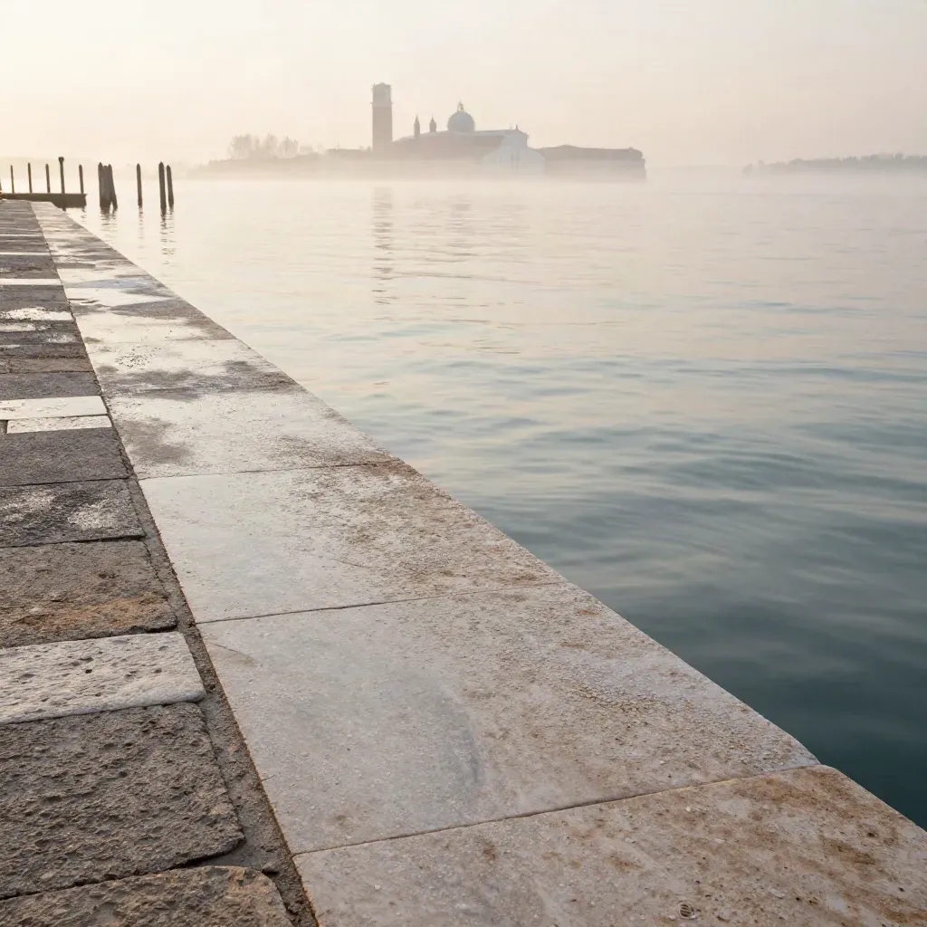 Riva veneziana in pietra d’Istria all’alba con acqua pallida e pali d’ormeggio lontani.